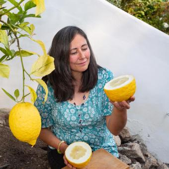 Woman holding cut open citron fruit next to a citron tree